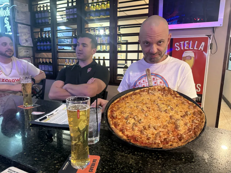 A slice scout at the Q's bar with a whole tavern-style pie and frosty beers, moments before the damage