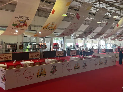 Red Caputo Cup competition floor with pizza stations, sponsor banners, ovens, and long white tables inside the Naples venue