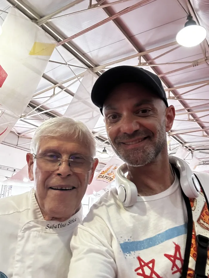 Patrick taking a selfie with a white-jacketed pizzaiuolo inside the Caputo Cup venue