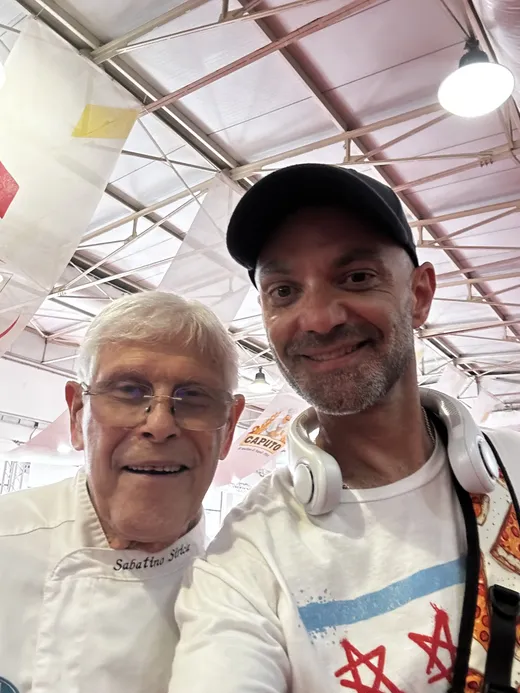 Patrick taking a selfie with a white-jacketed pizzaiuolo inside the Caputo Cup venue