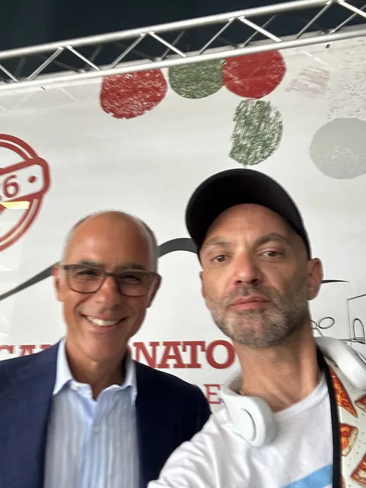 Patrick taking a selfie with a man in a suit in front of Caputo Cup signage