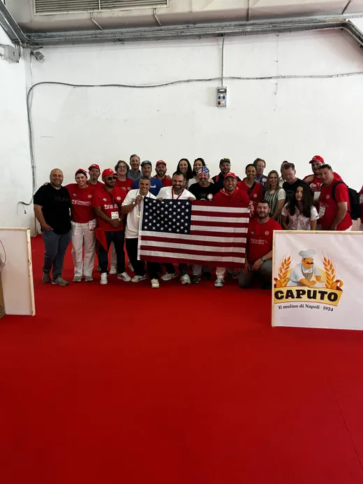 Group of Caputo Cup attendees posing on the red floor with an American flag and Caputo signage