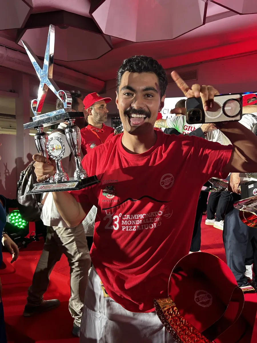 Smiling competitor in a red event shirt holding a trophy at the Caputo Cup