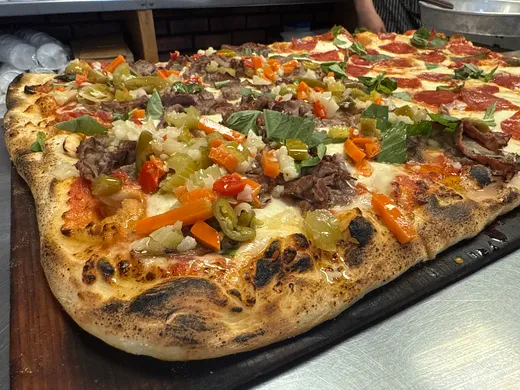 A square-cut Freddy's pan pizza piled with Italian beef and bright giardiniera on a wooden board