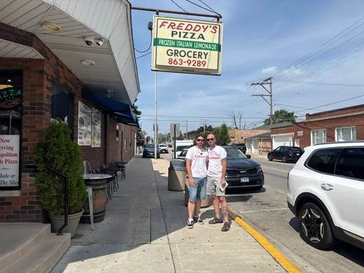 Two slice scouts on the sidewalk outside Freddy's Pizza under its corner sign in Cicero