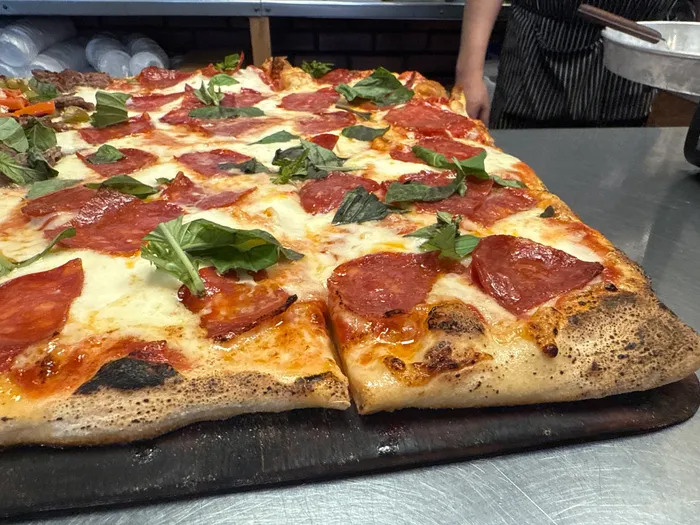 A square Freddy's pan pie with pepperoni cups and fresh basil, cheese browned at the edges