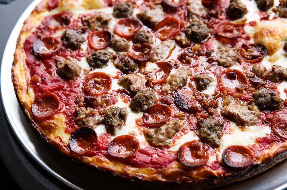 Close-up of a George's Deep Dish pie loaded with sausage chunks and pepperoni, crust edge browned and crisp