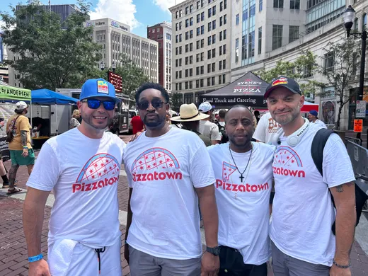 Four slice scouts in Pizzatown shirts on a brick street at the Indianapolis Pizza Festival