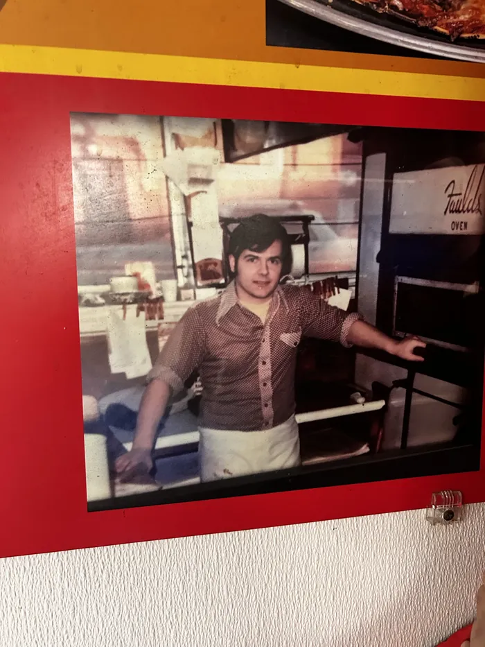 A framed 1970s photo at Pat's of a young pizzaiolo working the oven