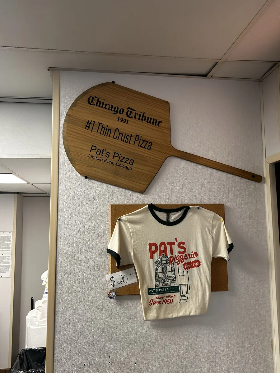 A vintage Pat's Pizza t-shirt and wooden pizza peel mounted on the wall at Pat's
