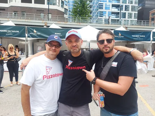 Three slice scouts arm in arm at Pizza City Fest, river towers behind them
