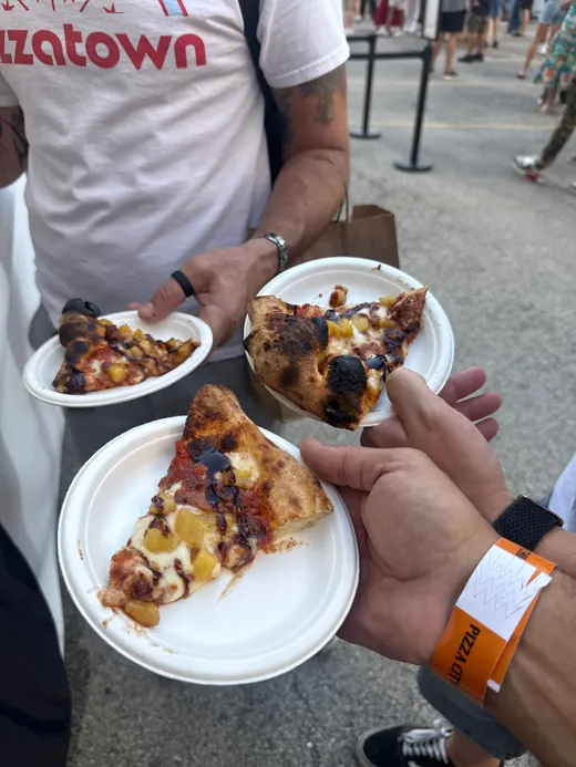 Two loaded tasting plates held up mid-festival, a wristband in frame