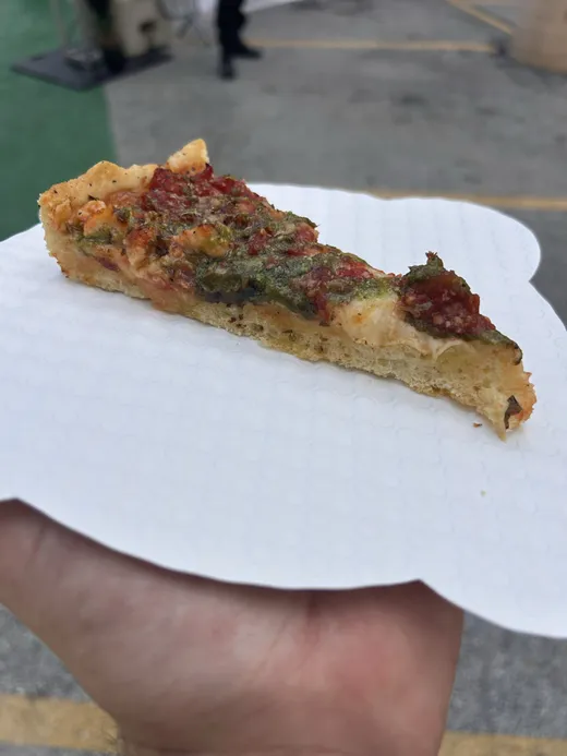 A thick caramelized pan slice with giardiniera held up on a napkin