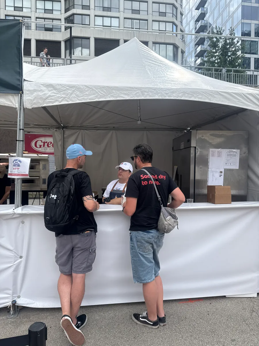 Fest-goers lining up at a white vendor tent at Pizza City Fest
