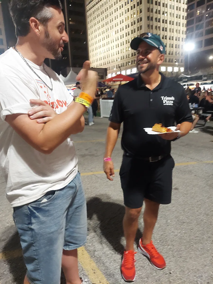 Two pizza guys talking shop over plates at the night market
