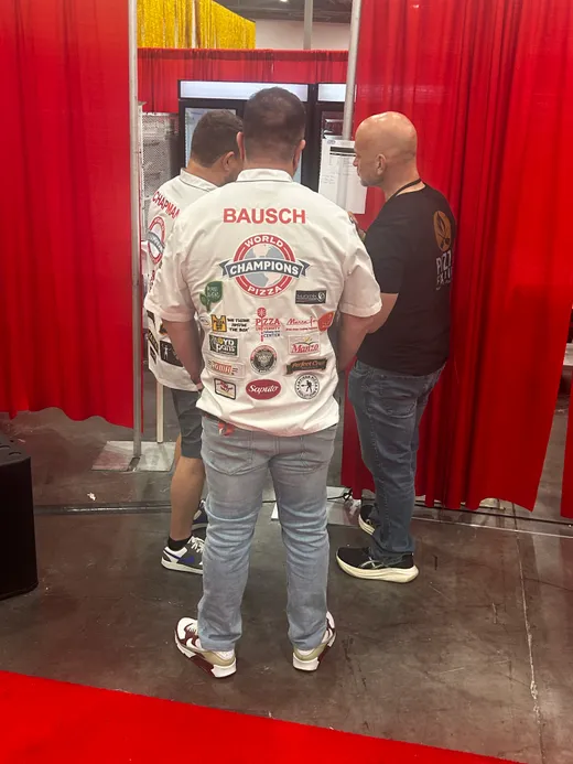 Two attendees talking by the red backstage curtains at Pizza Expo