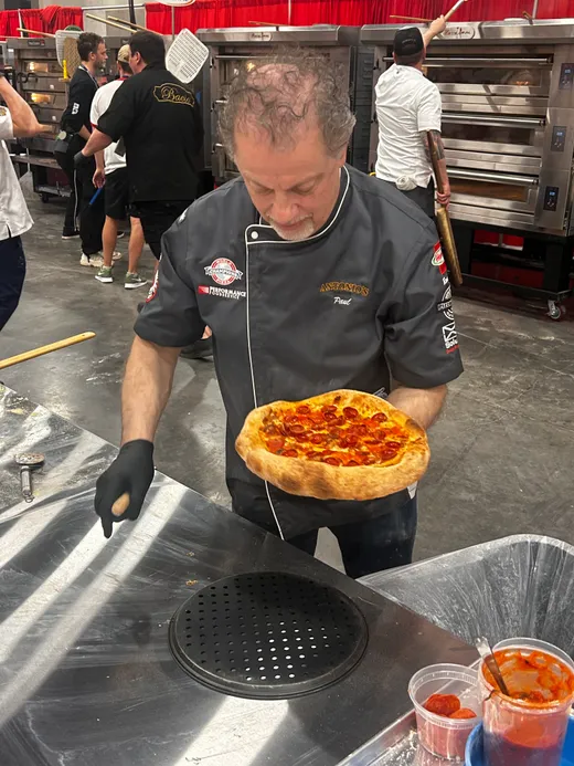 A chef boxing a tomato-topped pan pizza at the competition tables