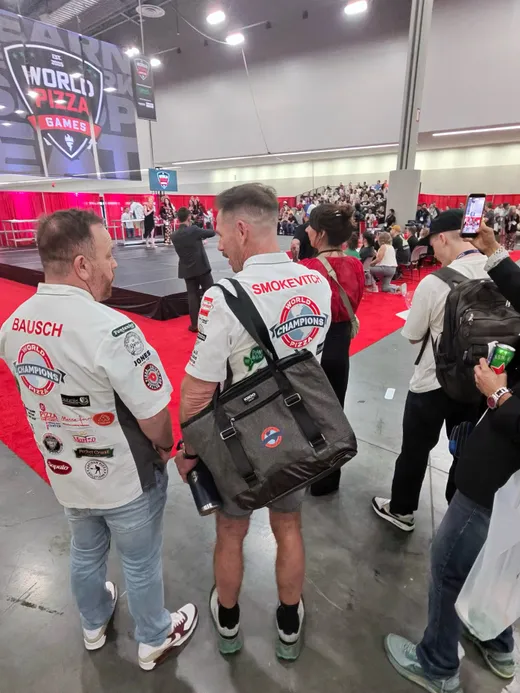 World Pizza Games competitors in patch-covered team jackets watching the floor
