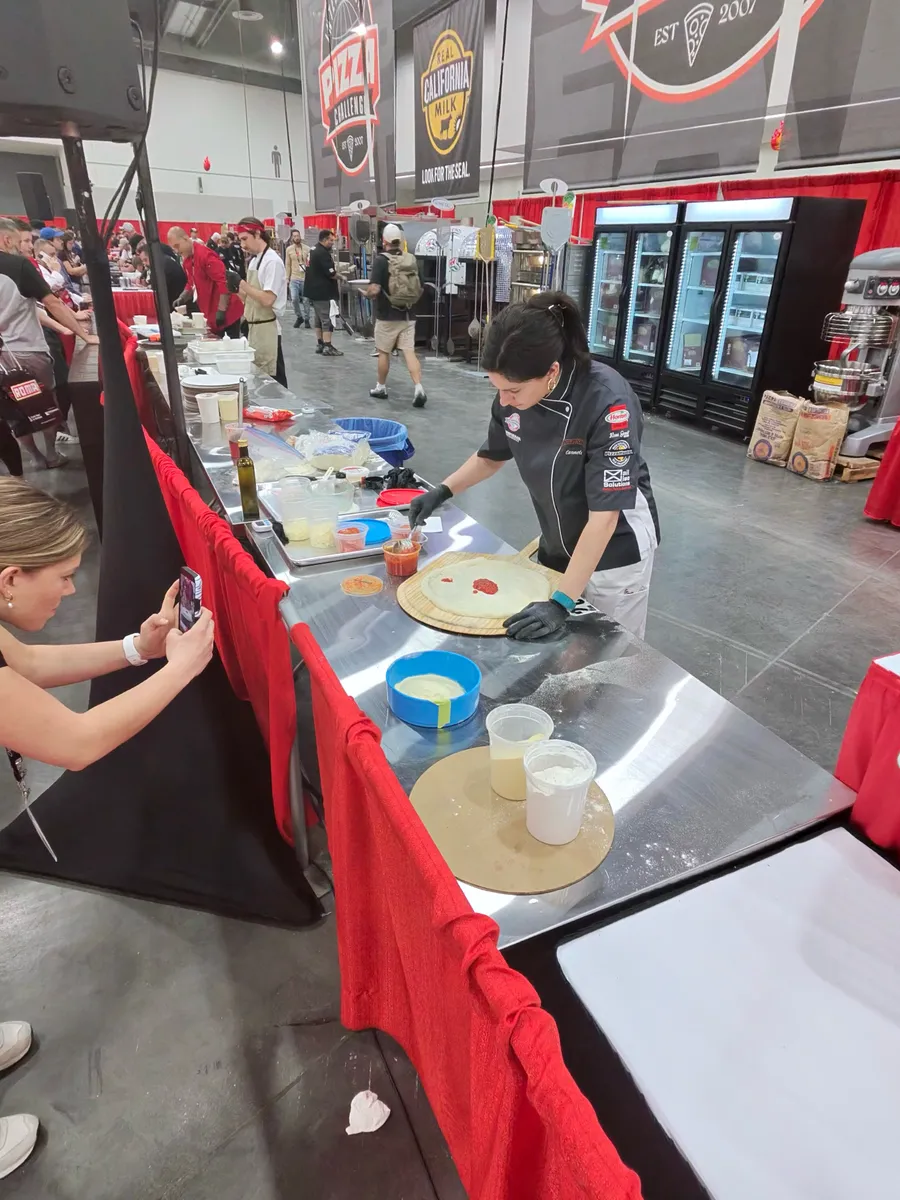 A competitor rolling dough at a long competition table draped in red