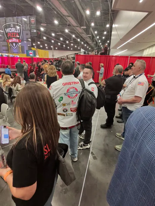Attendees in crew shirts threading through the Pizza Expo booth aisles