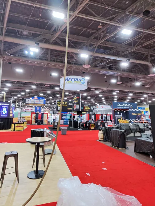 Wide view of the Pizza Expo hall, red carpet aisles and booth trusses overhead