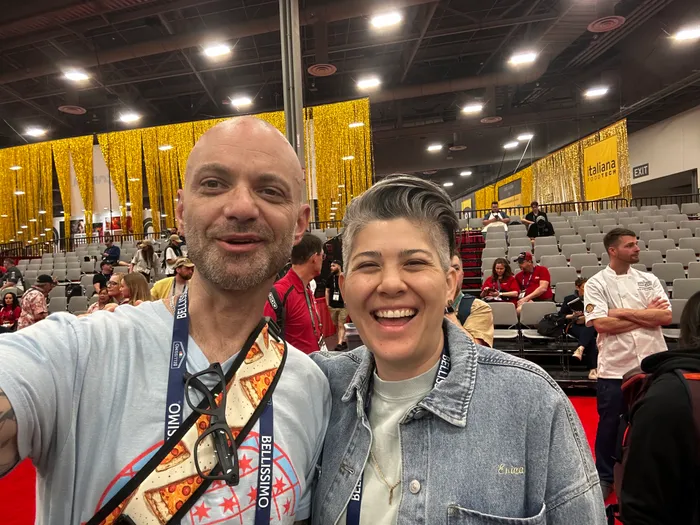 A slice scout and a fellow pizza obsessive laughing into a selfie in the Pizza Expo stands