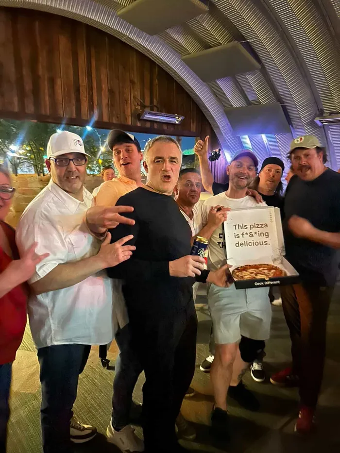 A late-night group photo, one member holding up a pizza box with a very enthusiastic verdict written on it