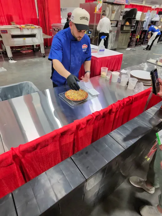 A competitor in a blue team shirt plating slices at the end of a competition table