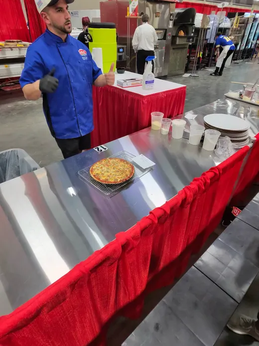 A vendor in blue serving a fresh pie at a tasting table with stacks of plates