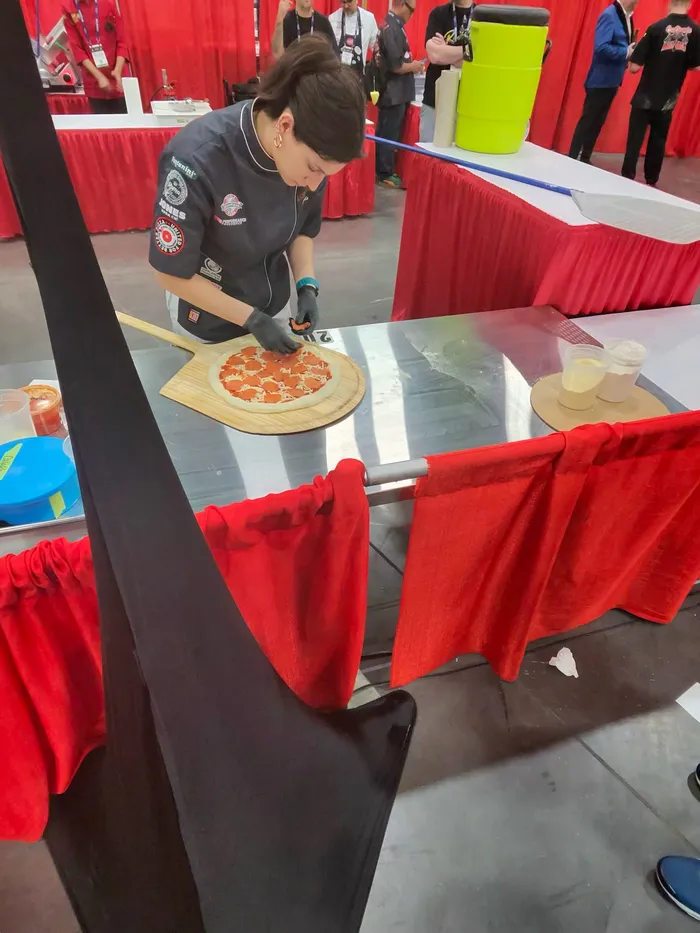 A competitor carefully topping a pizza at a competition station