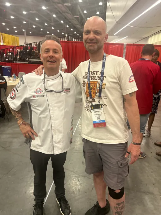A slice scout posing with a chef-coated pizzaiolo on the competition floor