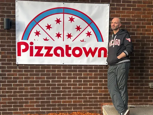 A slice scout standing proud next to the Pizzatown banner, hands in pockets