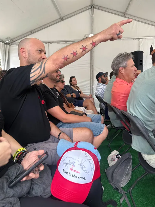 A slice scout with a Chicago-stars tattoo pointing at the screen during a pizza panel