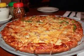 A golden tavern-style thin crust on a metal tray at Q's, red pepper flakes and table settings around it
