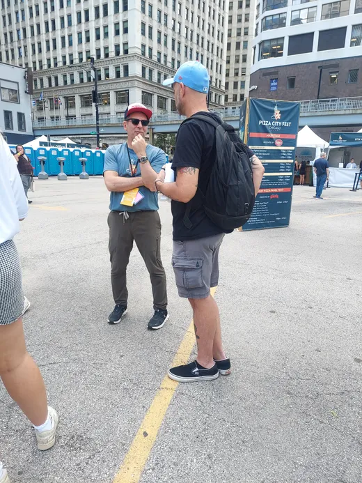 A festival conversation in progress: blue cap, backpack, full attention
