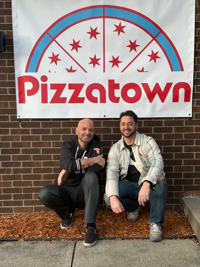The Viviribros sitting under the Pizzatown banner against a brick wall