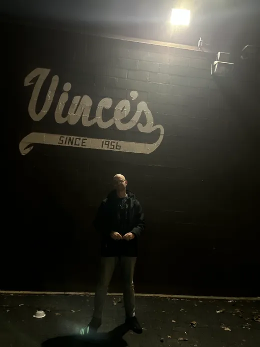 The glowing Vince's neon script sign over a South Side sidewalk at night