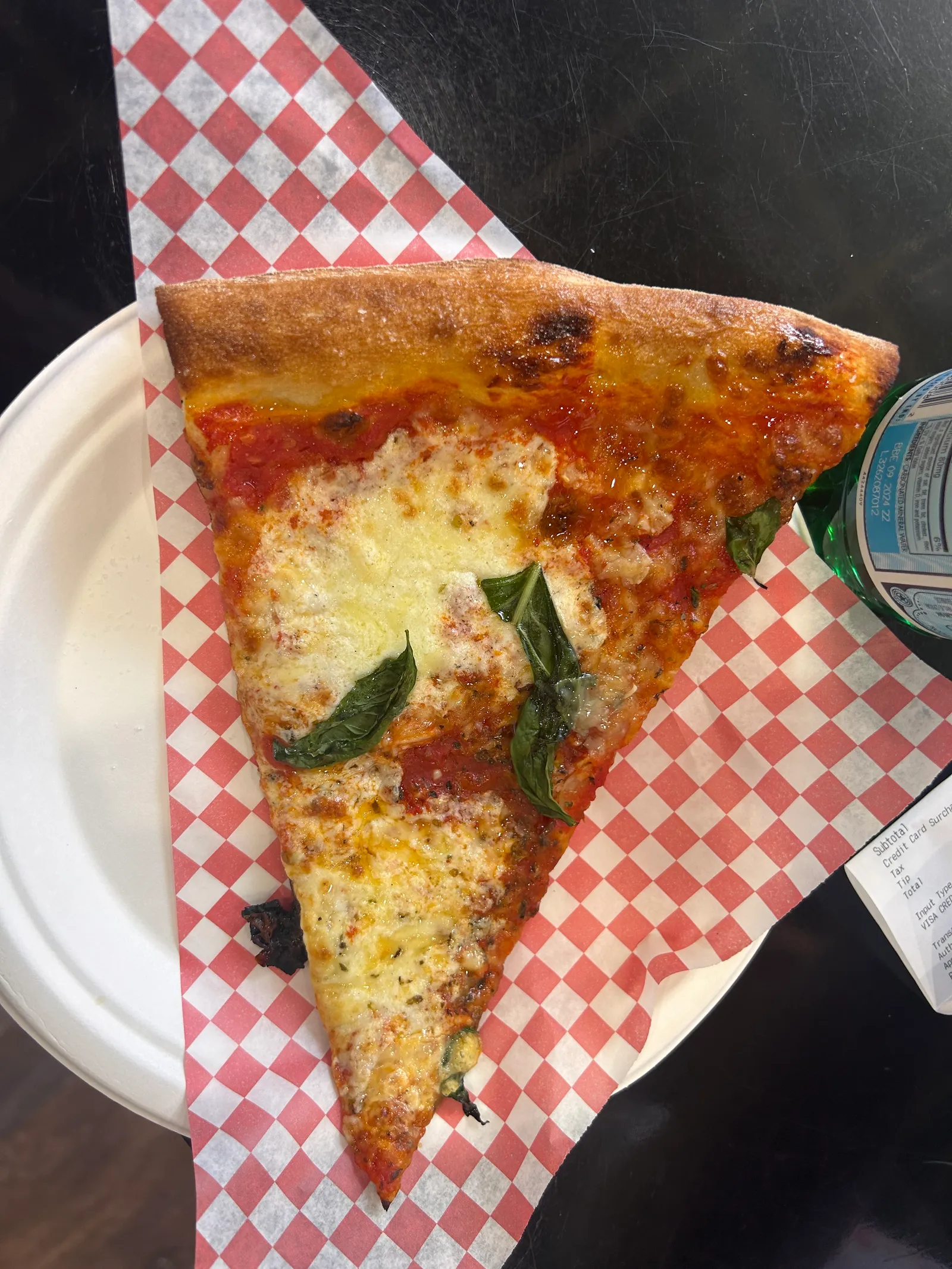 A wide Zaza's cheese slice with basil on red-checkered paper, tip folded just enough to hold