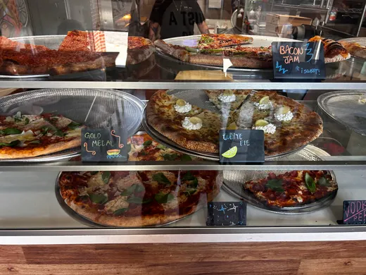 Whole pies lined up behind the counter glass at Zaza's, white pies and red pies labeled with little chalk tags